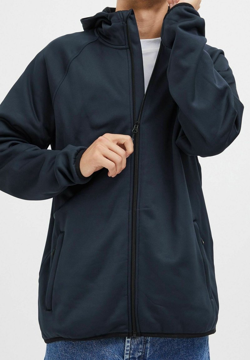 Tummansininen huppari, jossa on täysipitkä vetoketju, pitkät hihat, elastiset hihansuut ja kaksi sivutaskua. Sujuva pinta ja minimalistinen muotoilu.