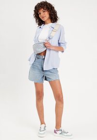 Sacoche à carreaux bleus et blancs, chemise à rayures bleu clair, t-shirt blanc, shorts en denim déchirés, baskets pastel avec des accents multicolores.