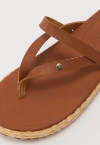 Ciabatte in pelle marrone con fasce incrociate, una soletta testurizzata e una suola in juta intrecciata con un accento metallico vicino alla base.