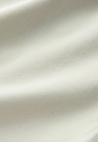 Gros plan d’un tissu lisse blanc cassé avec un motif subtil de tissage diagonal et de plis délicats créant des ombres douces.