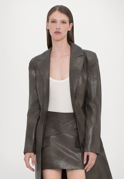 Brown leather oversized coat with shoulder pads, paired with a matching leather mini skirt. The inner top is cream-colored with a scooped neckline.