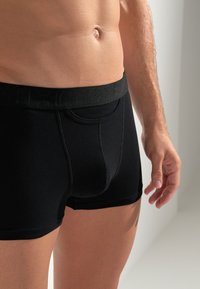 Schwarze Baumwoll-Boxershorts mit einem strukturierten elastischen Bund. Sie verfügen über eine körpernahe Passform und ein minimalistisches Design ohne zusätzliche Muster oder Akzente.