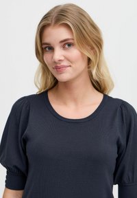 Tricou pulover de culoare bleu marin, cu un guler rotund și mâneci scurte puff, având un tricotaj texturat și detalii cu nasturi pe manșete.