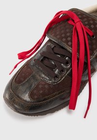Brown textured sneaker with worn leather details and black laces, featuring loose bright red shoelaces on a white background.