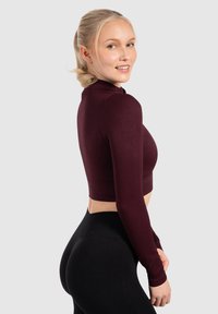 Burgundowy prążkowany crop top z długimi rękawami i stójką, zestawiony z czarnymi legginsami o wysokim stanie, oferującym dopasowany krój.