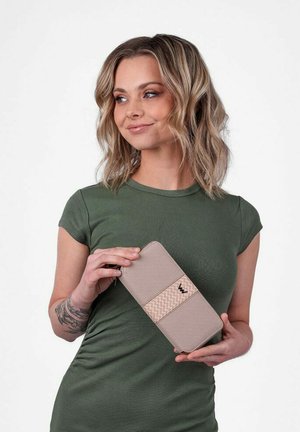 Beige peněženka s texturovaným, tkaným akcentním pruhem, se štíhlým obdélníkovým designem a hladkým textilním povrchem, kterou drží osoba.