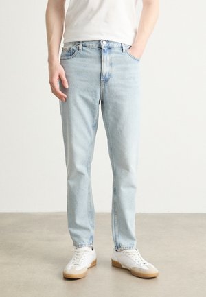 Light blue denim jeans with a straight cut, five-pocket design, and subtle fading. Paired with white sneakers, featuring light tan soles.