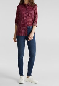 Camicia a quadri rossi con maniche arrotolate, abbinata a jeans skinny blu scuro e scarpe da ginnastica bianche. Tessuto liscio e vestibilità su misura.