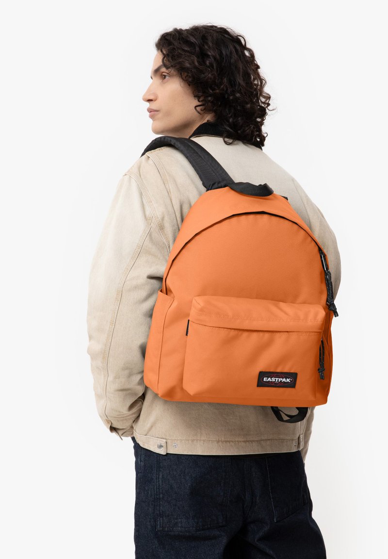 Zaino Eastpak arancione con design arrotondato, tasca frontale e spallacci neri. Realizzato in tessuto resistente con una texture liscia.
