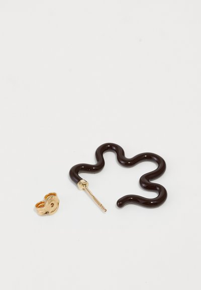 Dunkelbrauner, schlangenförmiger Ohrring aus glänzendem Material mit einem dünnen goldenen Stab, begleitet von einem kleinen goldenen Creolenohrring mit einem Gesichtsmotv.