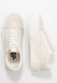 Para off-white sneakersy Vans z zamszowymi czubkami, bocznymi paskami i wzorzystym materiałem u góry, przedstawione z widoku z góry i z boku na białym tle.