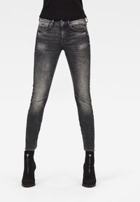 Jeans skinny negros con un lavado gris desgastado, que cuentan con bolsillos con cremallera y un diseño ajustado para una silueta elegante.