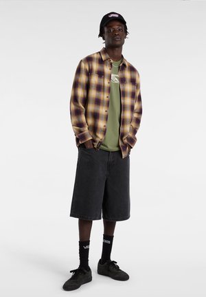 Skakternet flannel skjorte i lilla og guld, olivengrønt t-shirt, sorte denim shorts, sorte sneakers og Vans logo sokker.