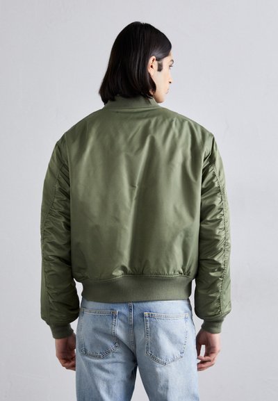 Chaqueta bomber verde oliva con una textura suave, puños y dobladillo acanalados, que presenta hombros acolchados y un dise�ño corto.