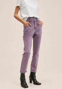 Jeans de mezclilla morados de cintura alta y ajuste relajado, con costuras en contraste, bolsillos laterales y un ligero ajuste en el tobillo, combinados con botas negras.