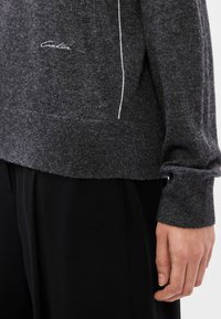 Grau gestreifter Wollpullover mit geripptem Saum und Bündchen, dezentem weißen Nähtdetail und kleinem Logo an der unteren Vorderseite.
