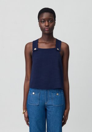 Top court sans manches bleu marine avec décolleté carré, bretelles épaisses avec accessoires en argent, associé à un pantalon en denim taille haute.