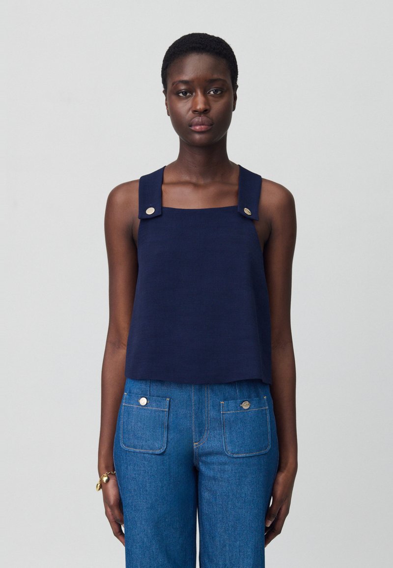 Top corto senza maniche di colore blu navy con scollo quadrato, spalline spesse con dettagli in metallo argentato, abbinato a pantaloni in denim a vita alta.