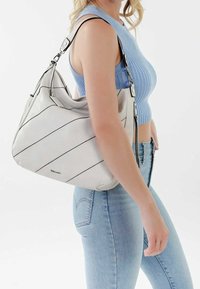 Stor vit läderaxelväska med svarta diagonala ränder, silverdetaljer och en mjuk textur, bärs på axeln mot en ljus bakgrund.