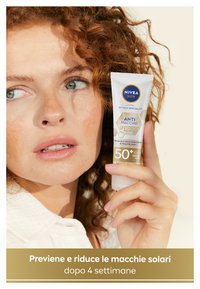 Tubo di crema solare NIVEA Sun anti-macchie tenuto in mano da una persona. Imballaggio in plastica bianca con accenti blu e oro. SPF 50+, etichettato per la protezione dai raggi UV.