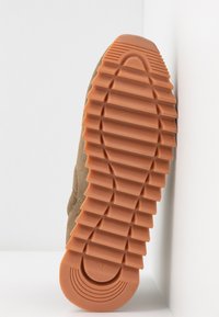 Basket en daim marron avec une semelle en caoutchouc orange texturée, présentant un motif nervuré et un accent circulaire au talon. Taille 37 indiquée.