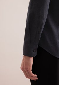 Camicia a maniche lunghe navy realizzata in tessuto testurizzato. Presenta polsini con bottone e orlo angolato, abbinata a pantaloni neri.