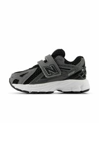 Chaussures de sport noires et grises avec une tige en mesh, une sangle Velcro ajustable et une semelle blanche avec un motif de grip texturé.