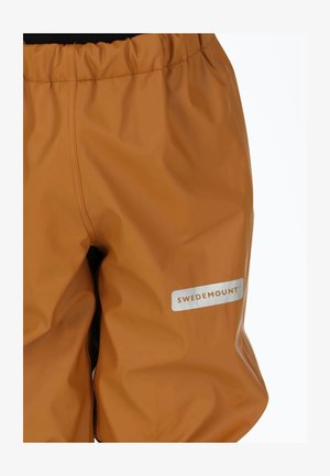 Wodoodporne pomarańczowe spodnie z elastycznym pasem. Na białej, prostokątnej naszywce znajduje się srebrne logo „SWEDEMOUNT”. Gładka, błyszcząca faktura.