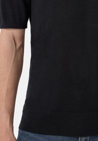 Svart kortärmad stickad tröja med en slät textur och ribbad fåll. Den har en rund halsringning och en figurnära silhuett.