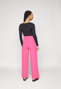 Zwarte lange mouwen top en roze wijde broek met een elastische tailleband, gezien vanaf de achterkant. Gladde stoftextuur en heldere kleurcontrasten.