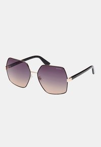 Ochelari de soare hexagonali cu lentile violet în degradé, ramă din metal aurie și brațe din plastic negru texturat cu un model subtil.