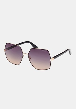 Ochelari de soare hexagonali cu lentile violet în degradé, ramă din metal aurie și brațe din plastic negru texturat cu un model subtil.