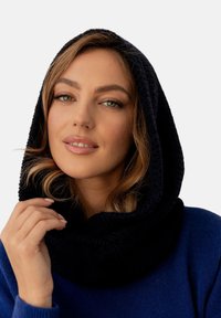 Czarny dzianinowy szalik z kołnierzem, wykonany z miękkiego, teksturowanego materiału, noszony nałożony na szyję. Modelka ma subtelne fale we włosach i na sobie niebieski sweter.