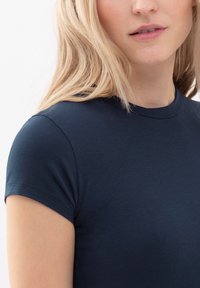 Námořnická modrá polokošile s krátkým rukávem a kulatým výstřihem, která má hladkou texturu a minimální detaily šití.