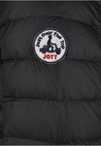Giacca nera imbottita con un patch ricamato rotondo con il testo "Just Over The Top" e "JOTT" sopra un grafico di uno scooter.