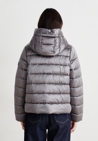 Veste rembourrée grise avec capuche, présentant des sections matelassées et un extérieur lisse et brillant. Le design comprend une longueur raccourcie et une coupe décontractée.