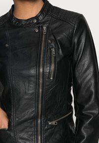 Veste de moto en cuir noir avec un col matelassé, des zippers diagonaux et plusieurs poches à fermeture éclair pour la fonctionnalité.