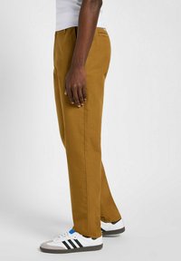 Brązowe bawełniane spodnie z prostą nogawką, z bocznymi kieszeniami i zapinaną na guzik tylną kieszenią, w połączeniu z białymi i szarymi trampkami.