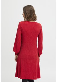 Röd klänning med en texturerad stickning, med långa puffärmar och en klassisk rund halsringning, som faller till mitten av låret.