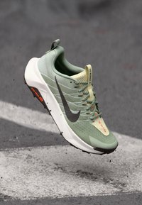 Zelená bežecká topánka Nike s vystuženým zvrškom z textilu, tmavosivým logom Swoosh, bielou podrážkou, šnúrkami a výrazným opätkom. Obsahuje štruktúrované detaily a akcenty loga.