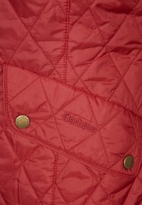 Czerwona kurtka pikowana z diagonalnymi wzorami w diamenty, zapinana na zatrzaski, z haftowanym logo "Barbour" z przodu.