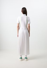Abito polo bianco con gonna plissettata, dettagli verdi sui lati e sneakers bianche con accenti verdi. Tessuto dalla trama liscia.
