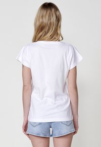 T-shirt en coton blanc avec des manches courtes légèrement évasées et un col rond, associé à un short en denim clair.