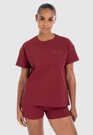 Burgunderfarvet bomulds sæt bestående af en T-shirt med korte ærmer og matchende tætsiddende shorts. Skjorten har en diskret logo detalje på brystet. Glat tekstur.