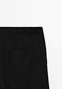 Bukser med sort elastisk linning og en stor rektangulær baglomme på højre side mod en hvid baggrund.