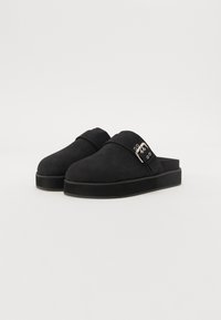 Crne cipele na slip-on napravljen od mekog antilopa, s zaobljenim vrhom i trakicom s srebrnom kopčom sa strane. Dizajn ravnog potplata.