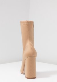 Bottine beige avec une finition lisse et mate, couture en relief le long de la couture, et un talon carré large et haut.