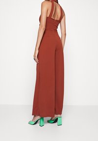 Mono de color óxido con un torso ajustado, diseño de pierna ancha y espalda descubierta. Combinado con sandalias de tacón cuadrado verdes.