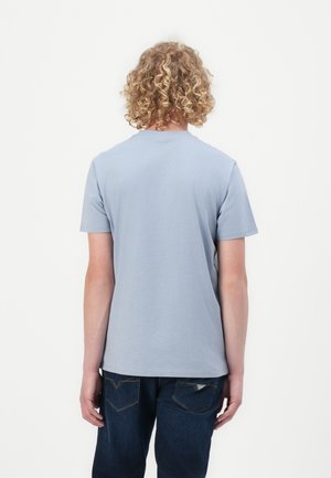Lys blå bomulls t-skjorte med korte ermer og rund hals, vist fra baksiden. Brukt sammen med mørkeblå jeans.