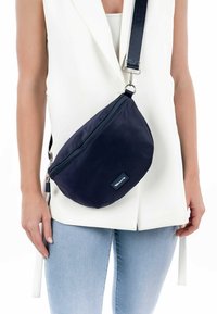 Borsa a tracolla in nylon blu navy con design curvo. Caratterizzata da una zip superiore e una tracolla regolabile. Piccola etichetta con logo sul davanti.